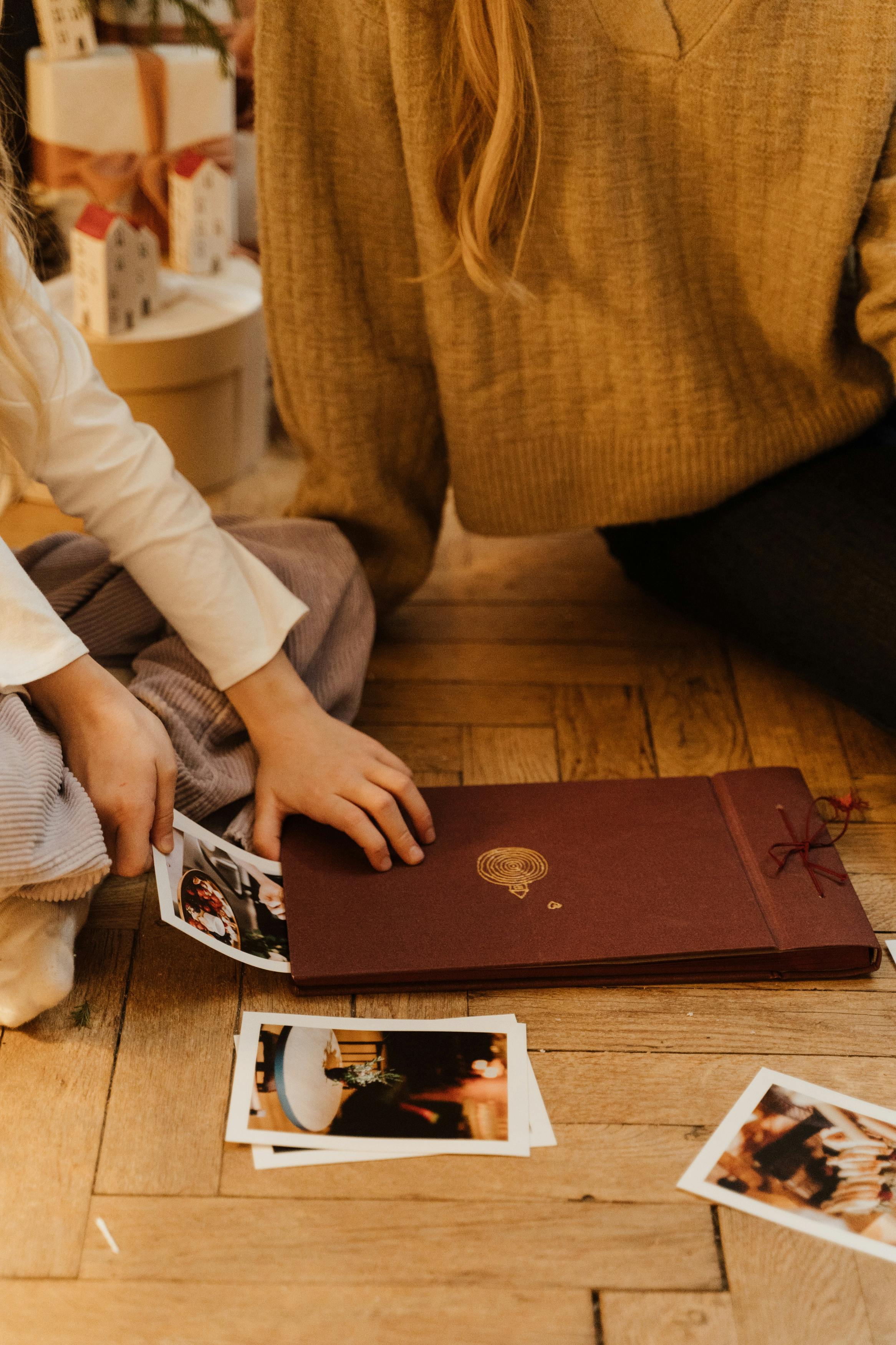 A kid removing photos from a book with an adult sitting beside them | Source: Pexels