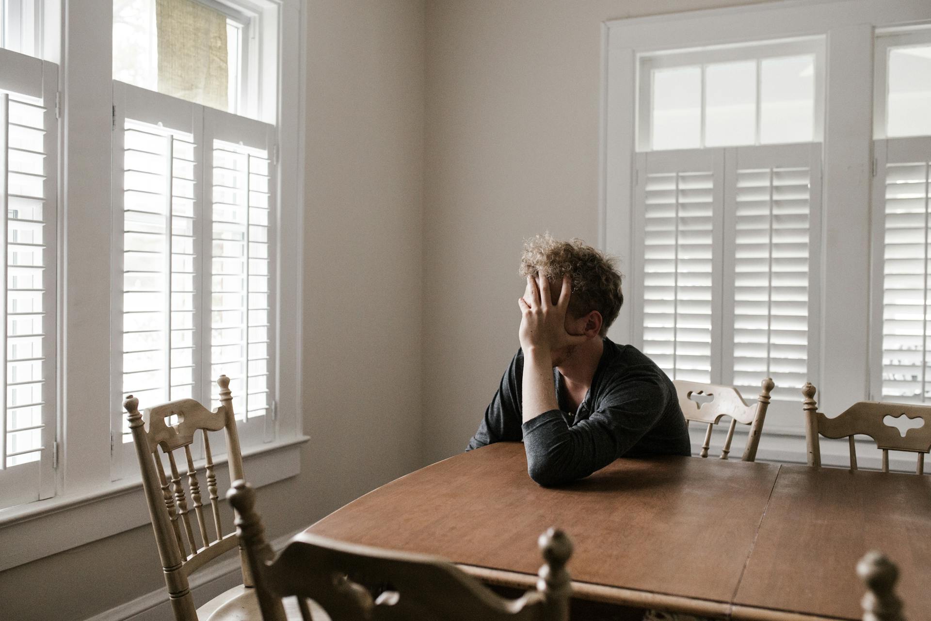 A sad man leaning on a brown wooden table | Source: Pexels