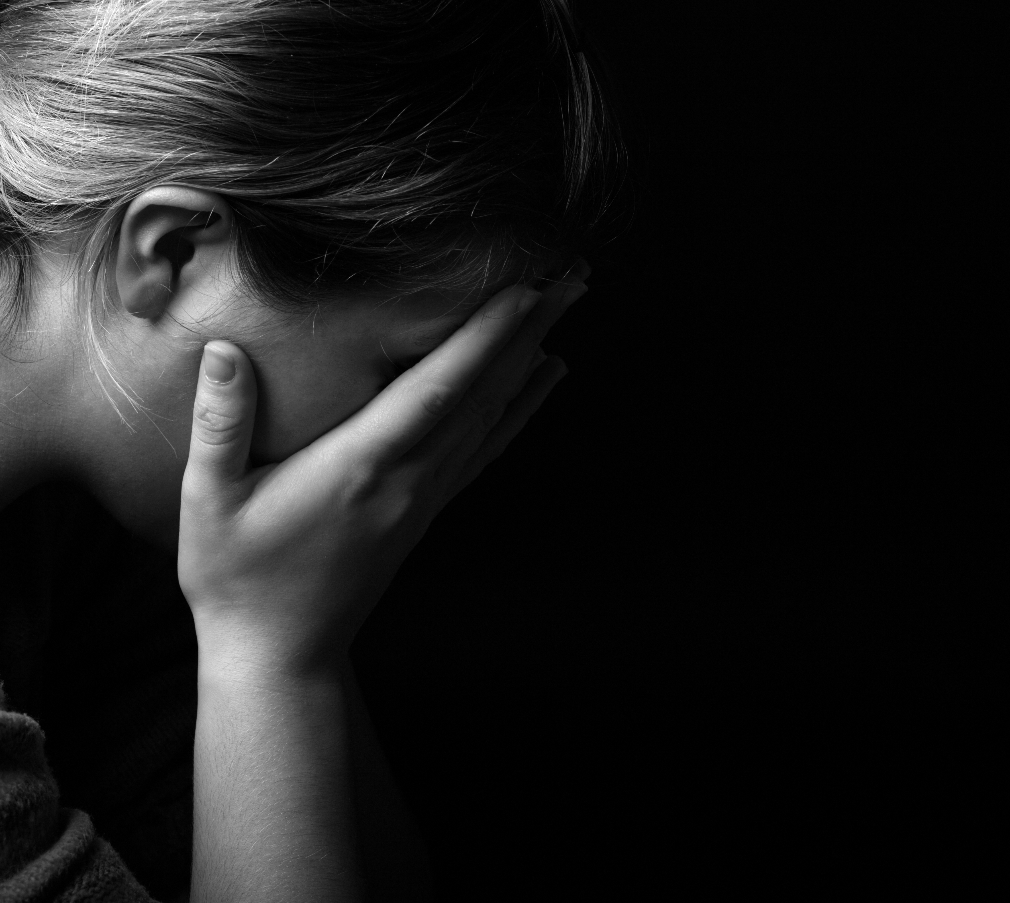 Woman covering her face in despair in the dark | Source: Shutterstock